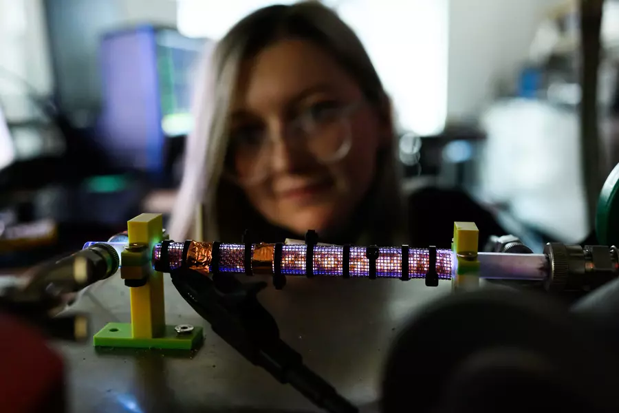 A 12-inch sized tube glows blue and white, with Lanie McKinney blurry in background.